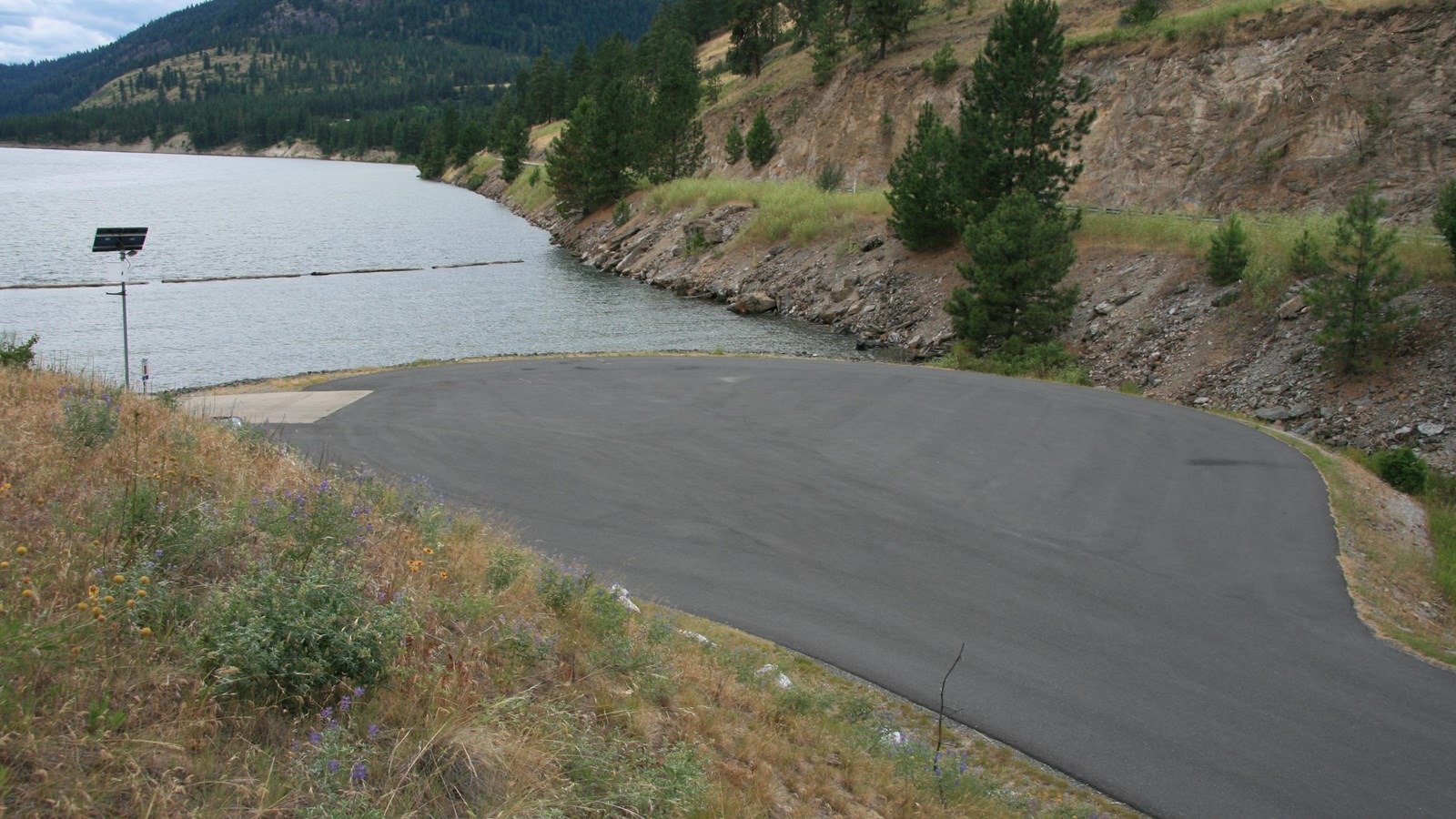 A paved access road descends to the paved boat launch adjacent to a cut bank on the shore.