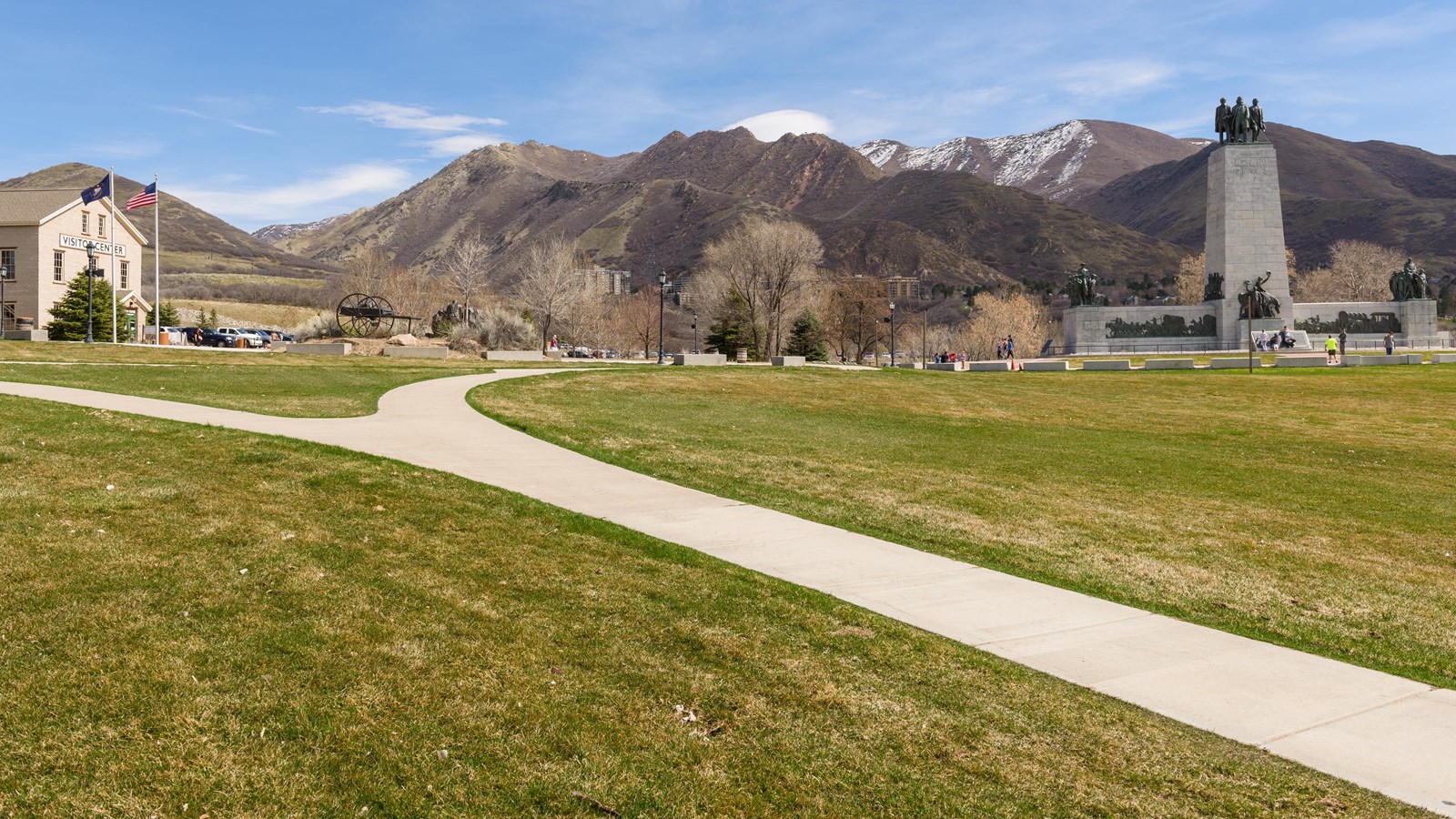 A sidewalk splits a grassy lawn and divides to two distant buildings.