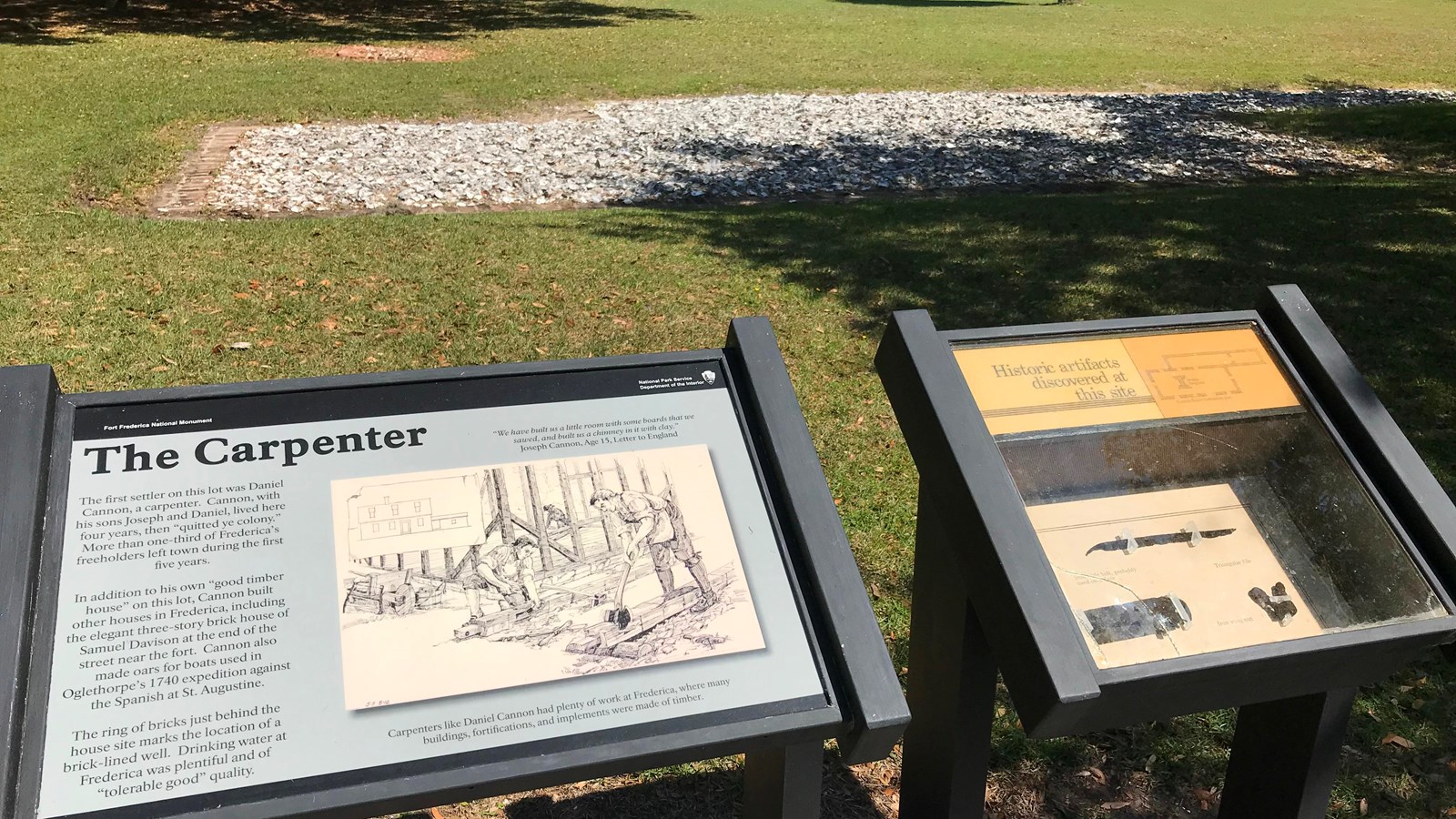 Display with text and artifacts in a shadowbox with foundation ruins and grassy area behind