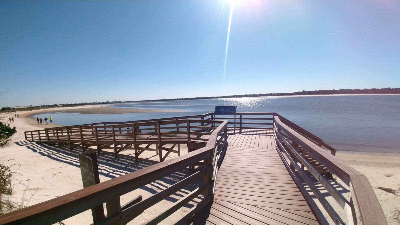 Boardwalk with a ramp and stairs. One exhibit sign, sunny sky, beach, low tide