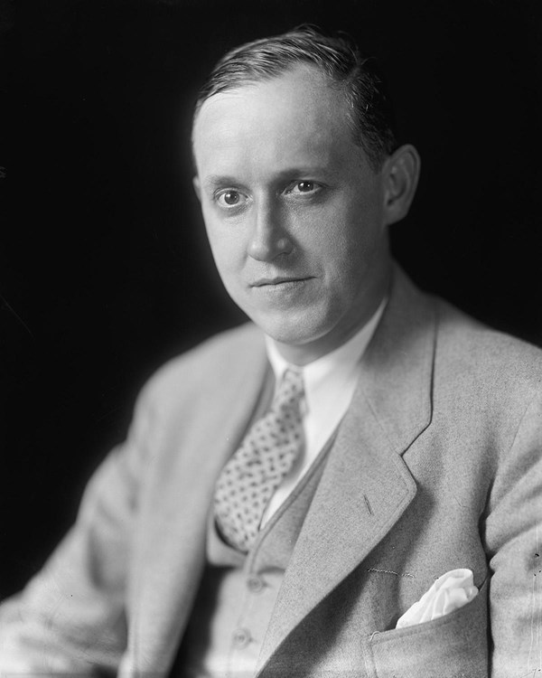 A seated man wearing a light suit and tie.