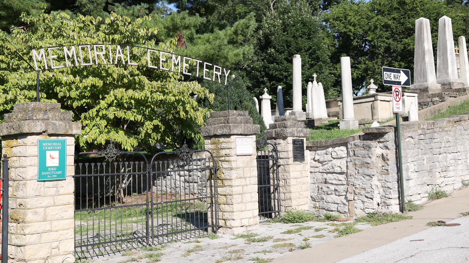 Black gate between two stone pillars, with white gravestones in the background