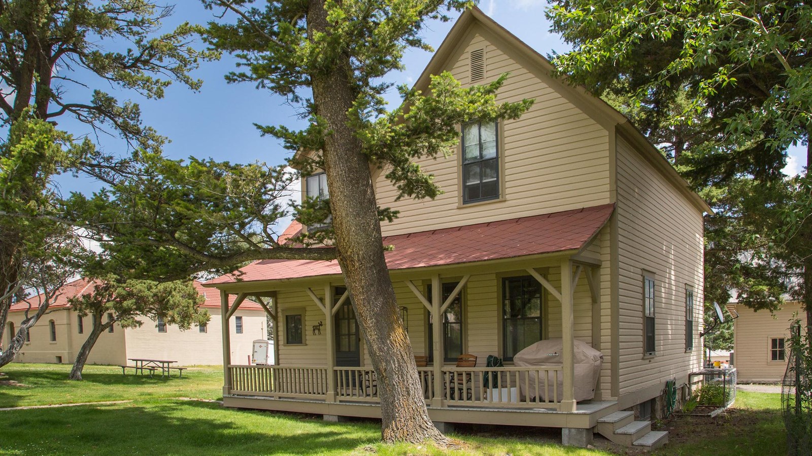 A historic building with pale, yellow siding, a red shingled roof, and a porch.