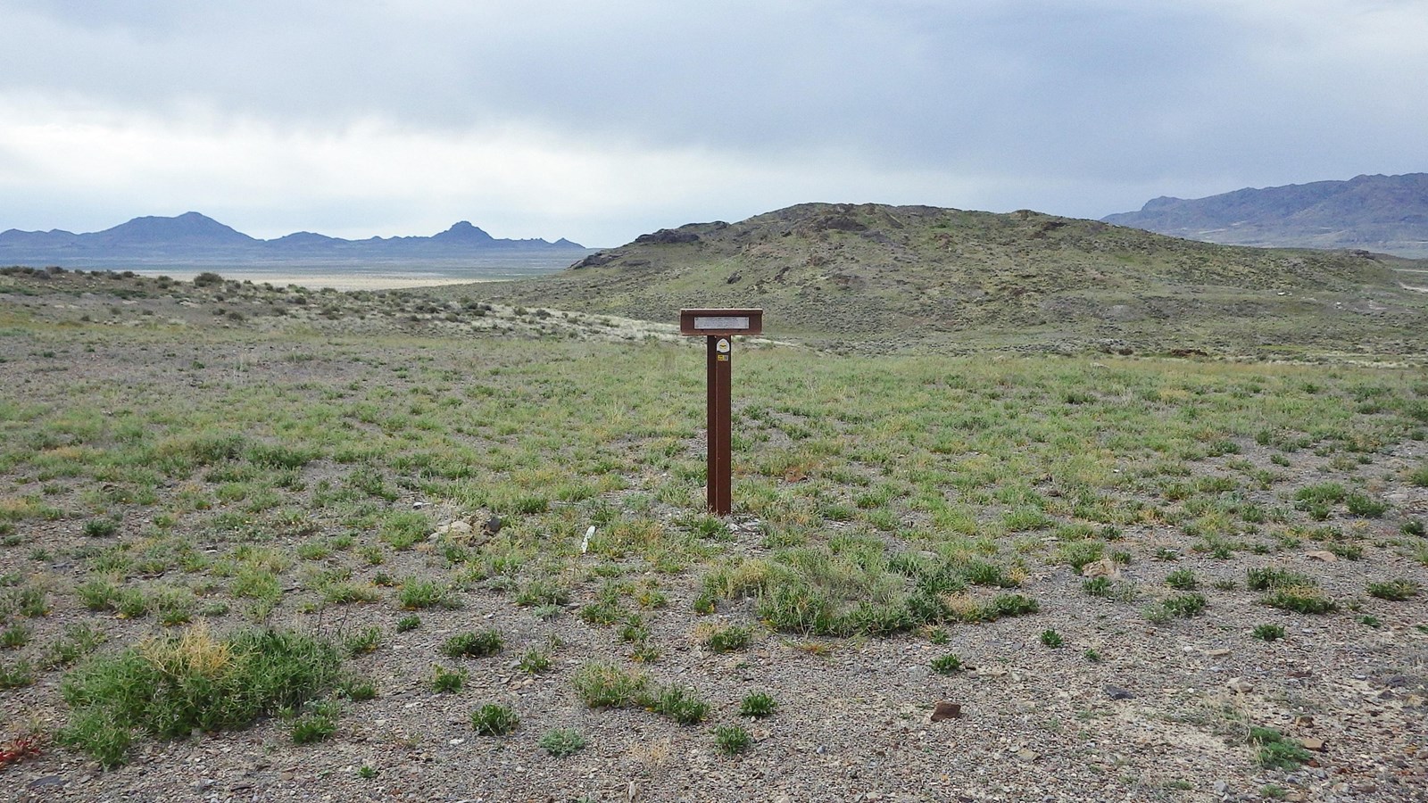 Wayside exhibit and trail marker on gravel plain beneath clear sky near Pilot Peak.