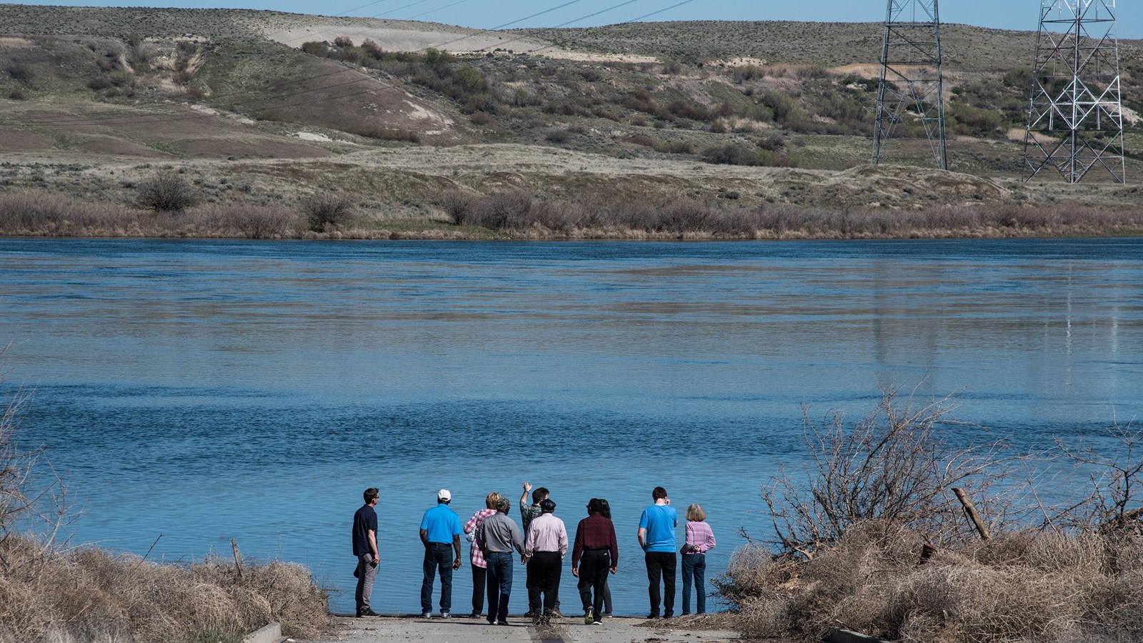 Color photograph of a group of six people at the bottom of a ramp looking across a river.
