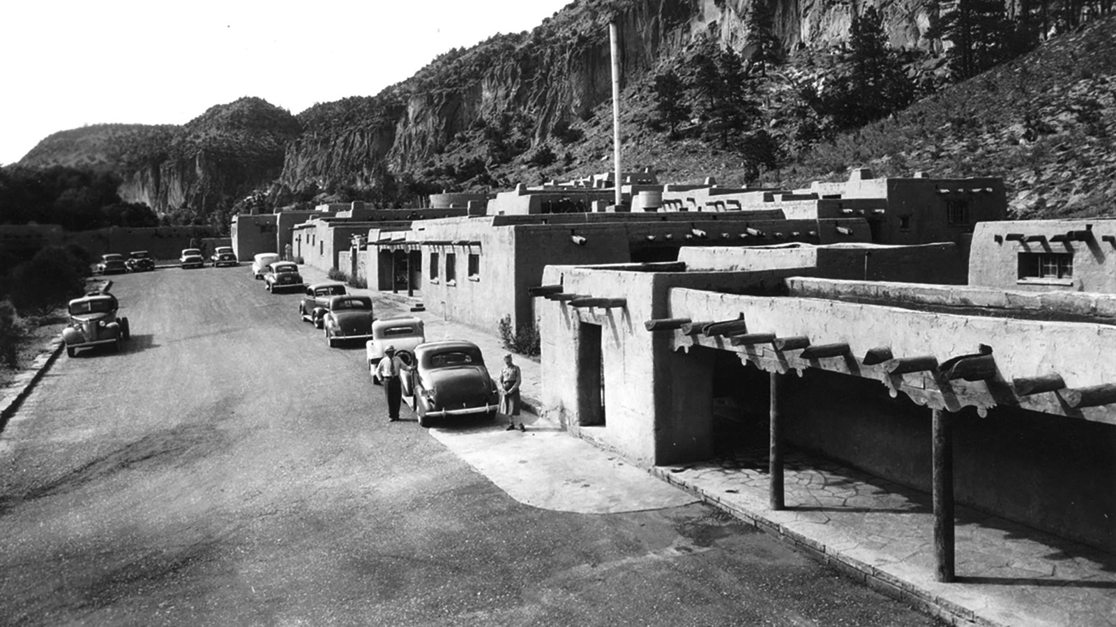 stone building surround a dirt parking lot with old cars