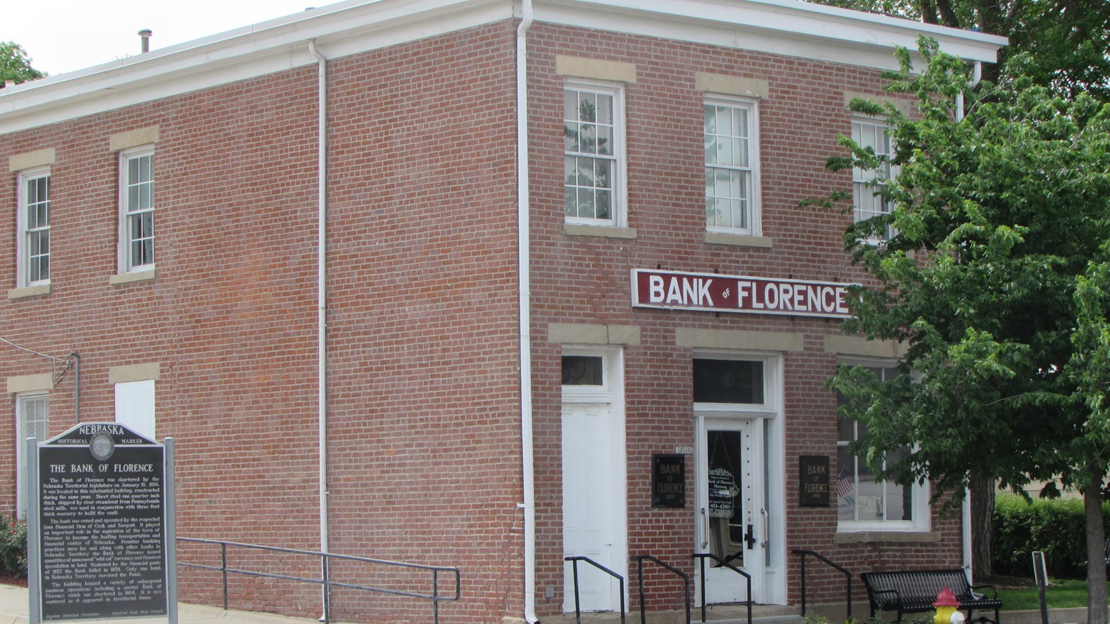 Two-story brick building with low hipped roof. Two doors and large window on main level.