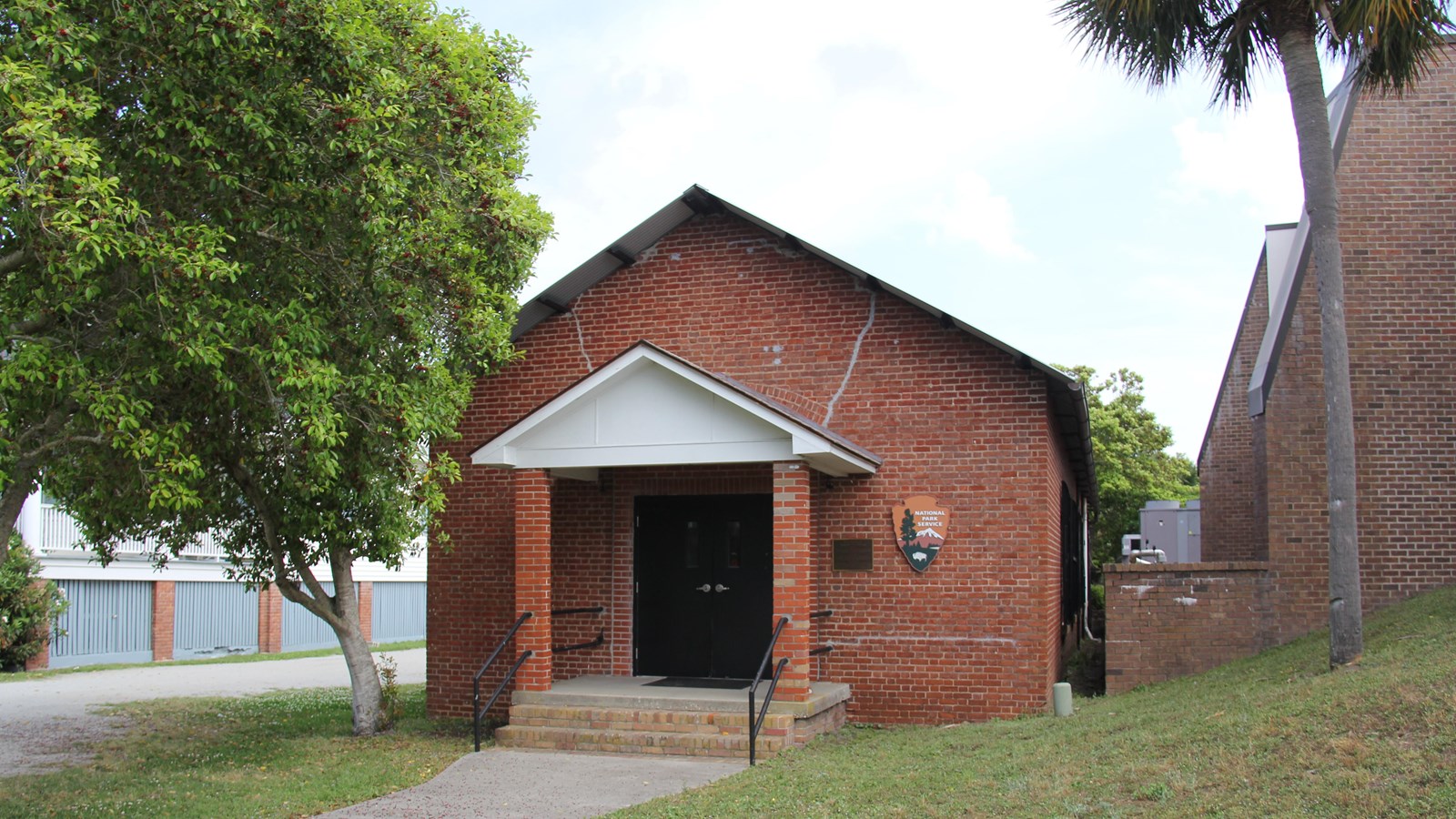 Brick one story building with gable entrance flanked by trees