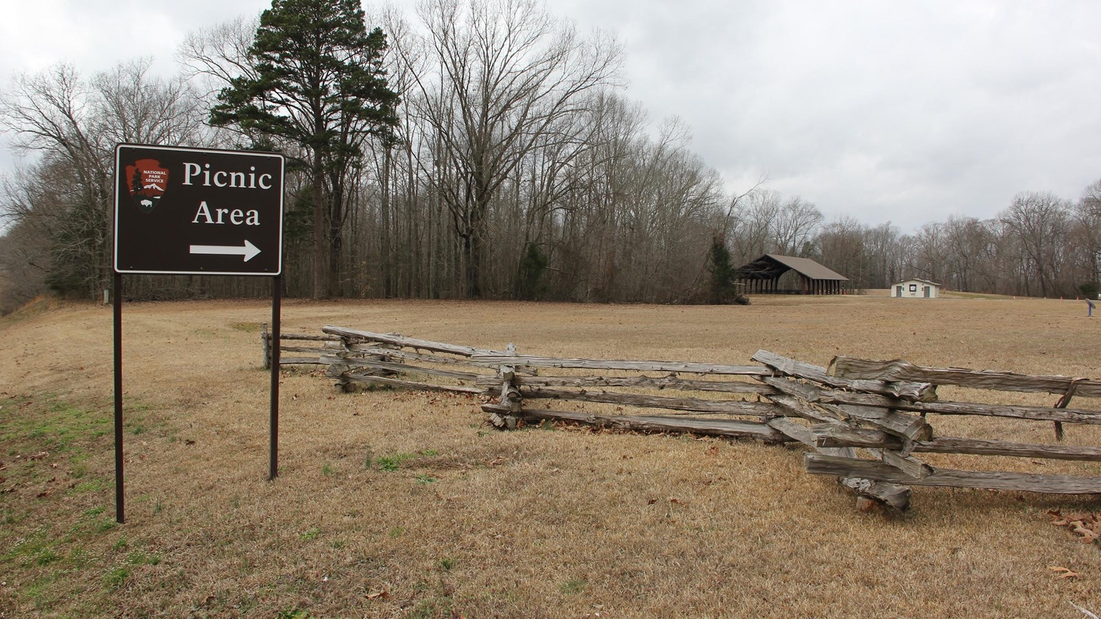 Brown sign with wooden pavilion in the background. 