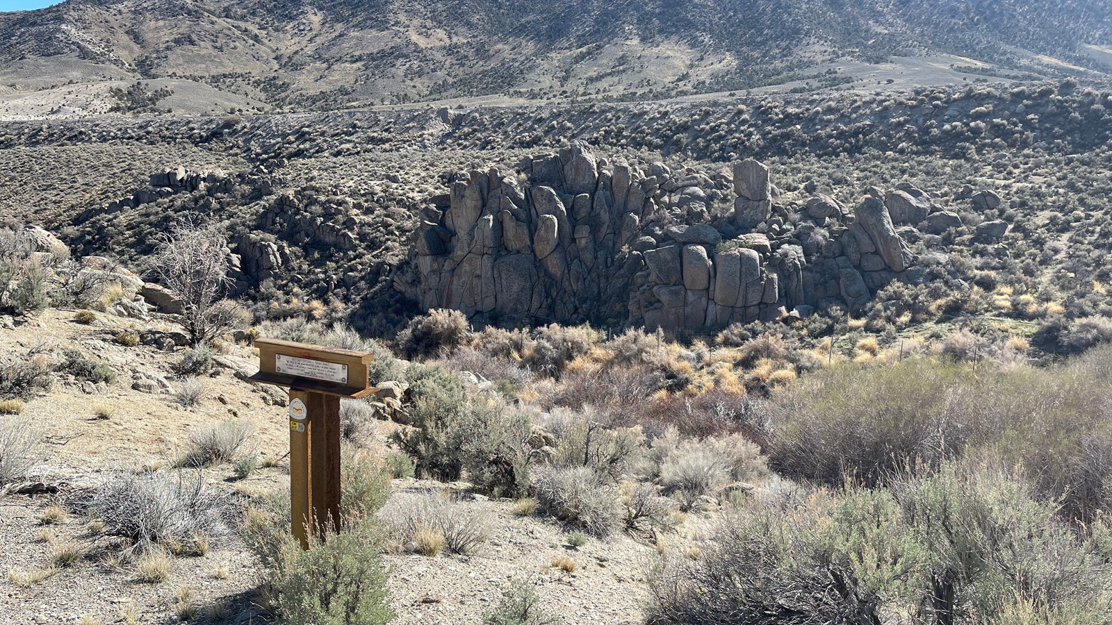 Ravine with shrubs, willows, rock columns, trail marker, hillside and freeway above nearby.
