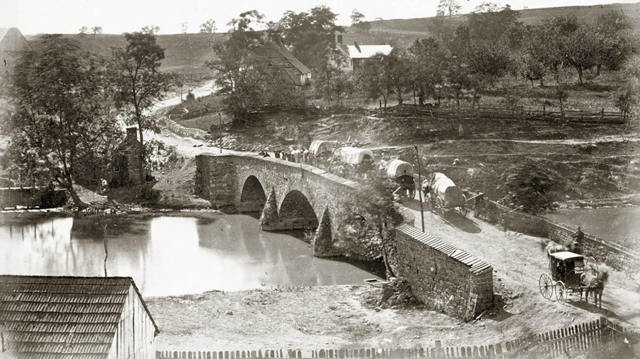 black and white photo of a stone bridge over a creek