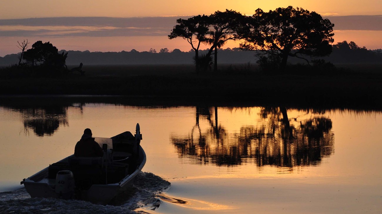 boat on water at dawn with tree reflected in water