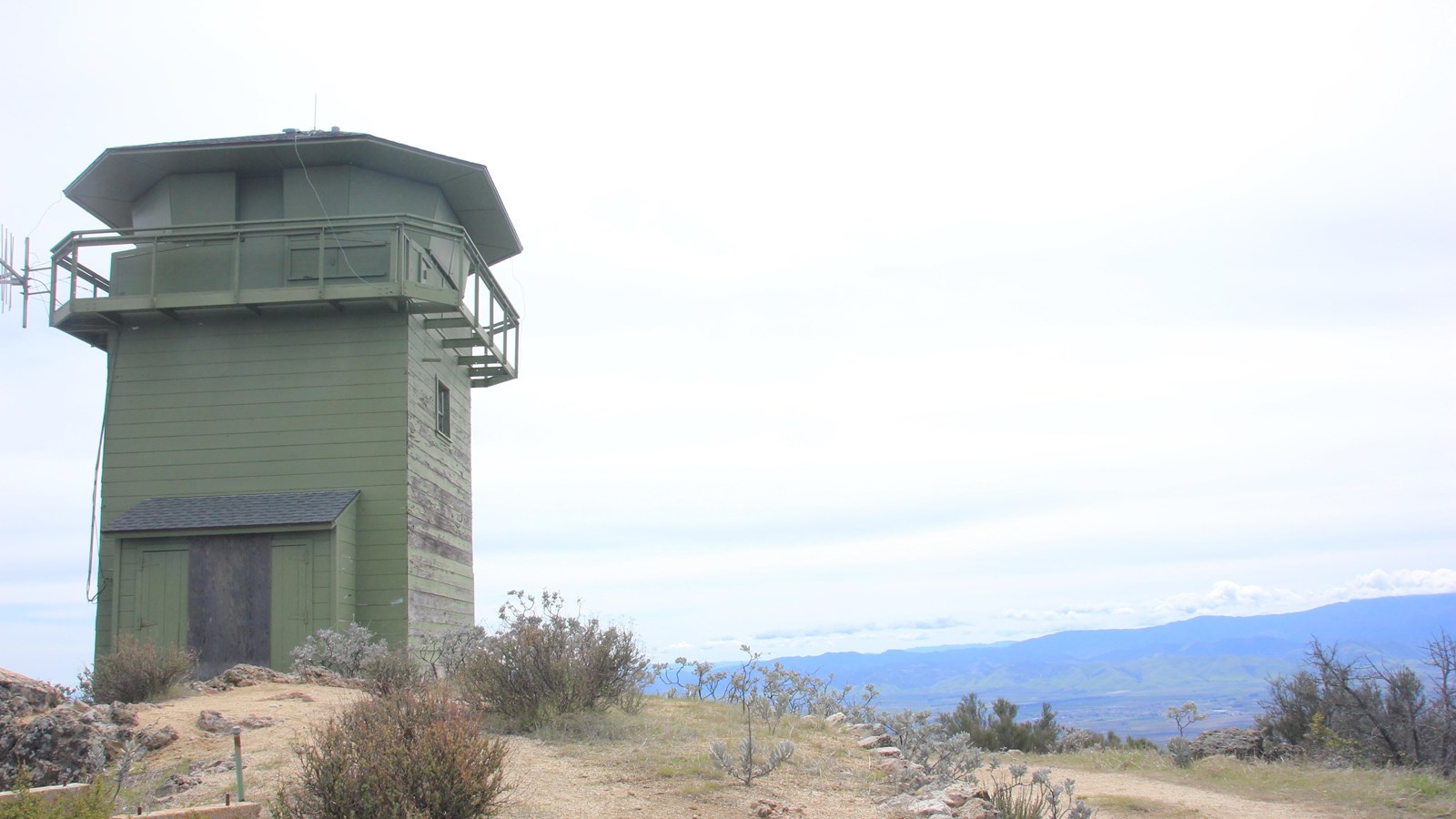 Green fire lookout tower on North Chalone Peak, surrounded by shrubs and mountain views.