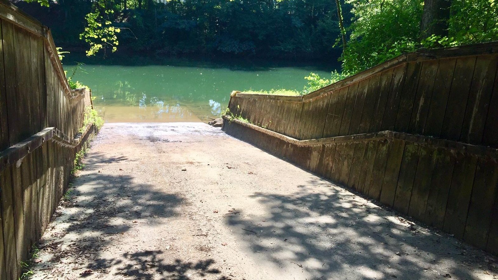 Looking down ramp with retaining walls on either side and wooded shoreline across river.