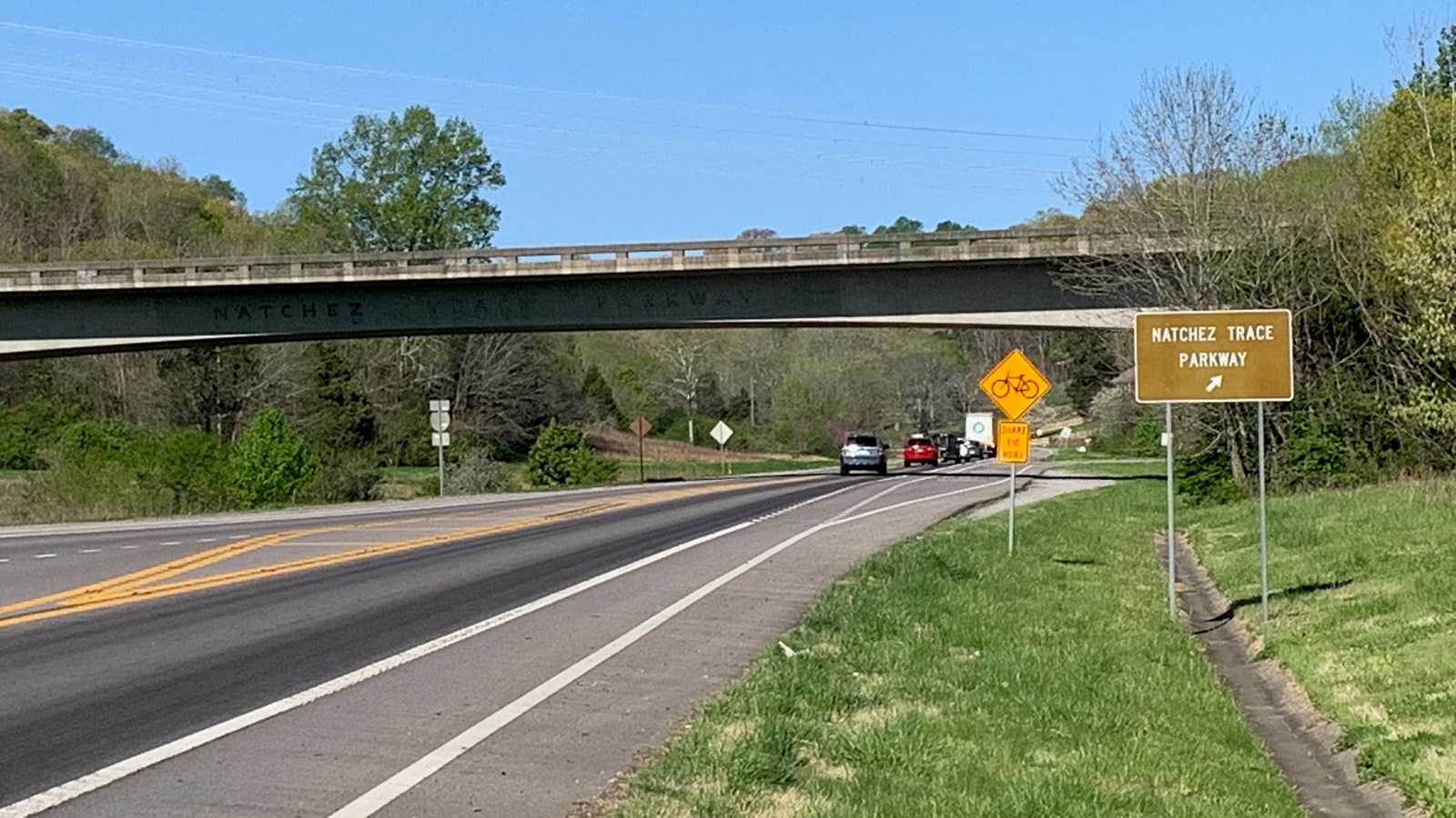 A two lane road with an overpass and a directional sign pointing to the ramp.