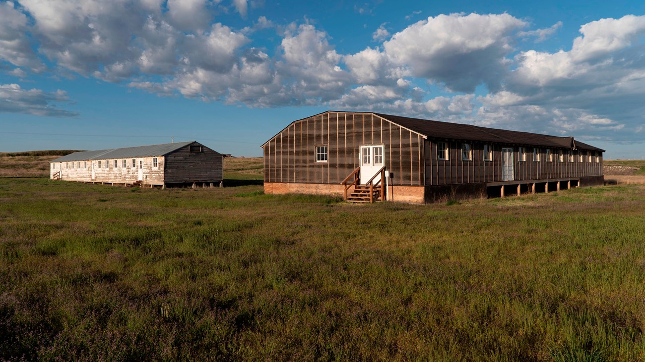 A historic mess hall and barracks sit in a grassy field at Minidoka.