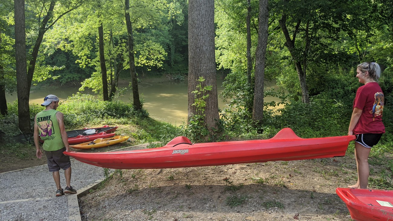 Two people carrying a red kayak down to the river