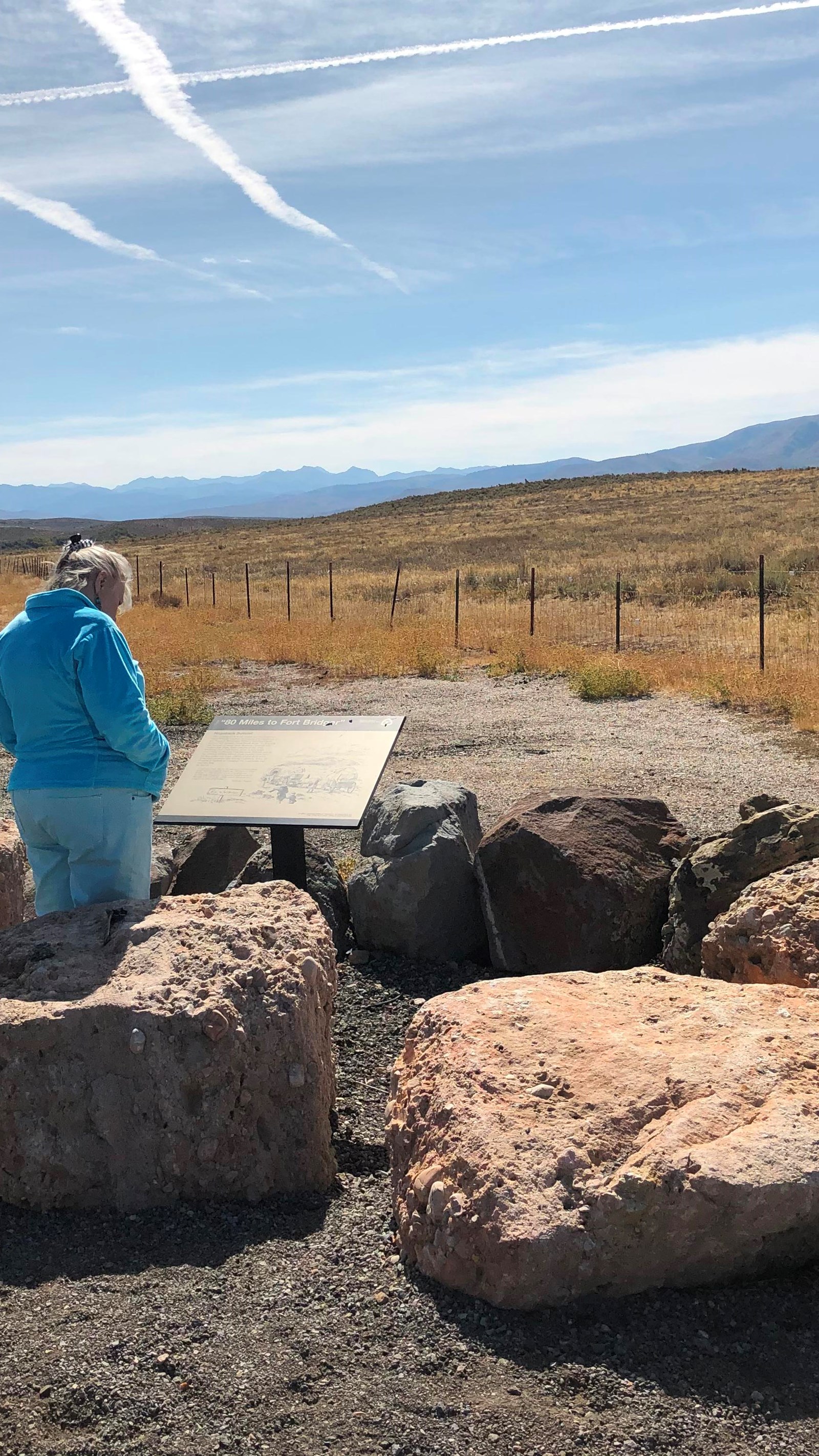 a woman reads a wayside sign on the side of a highway