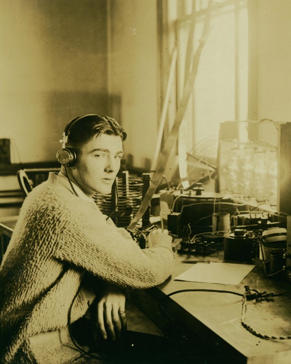 A 1921 photograph depicts a young man at a table operating radio equipment.