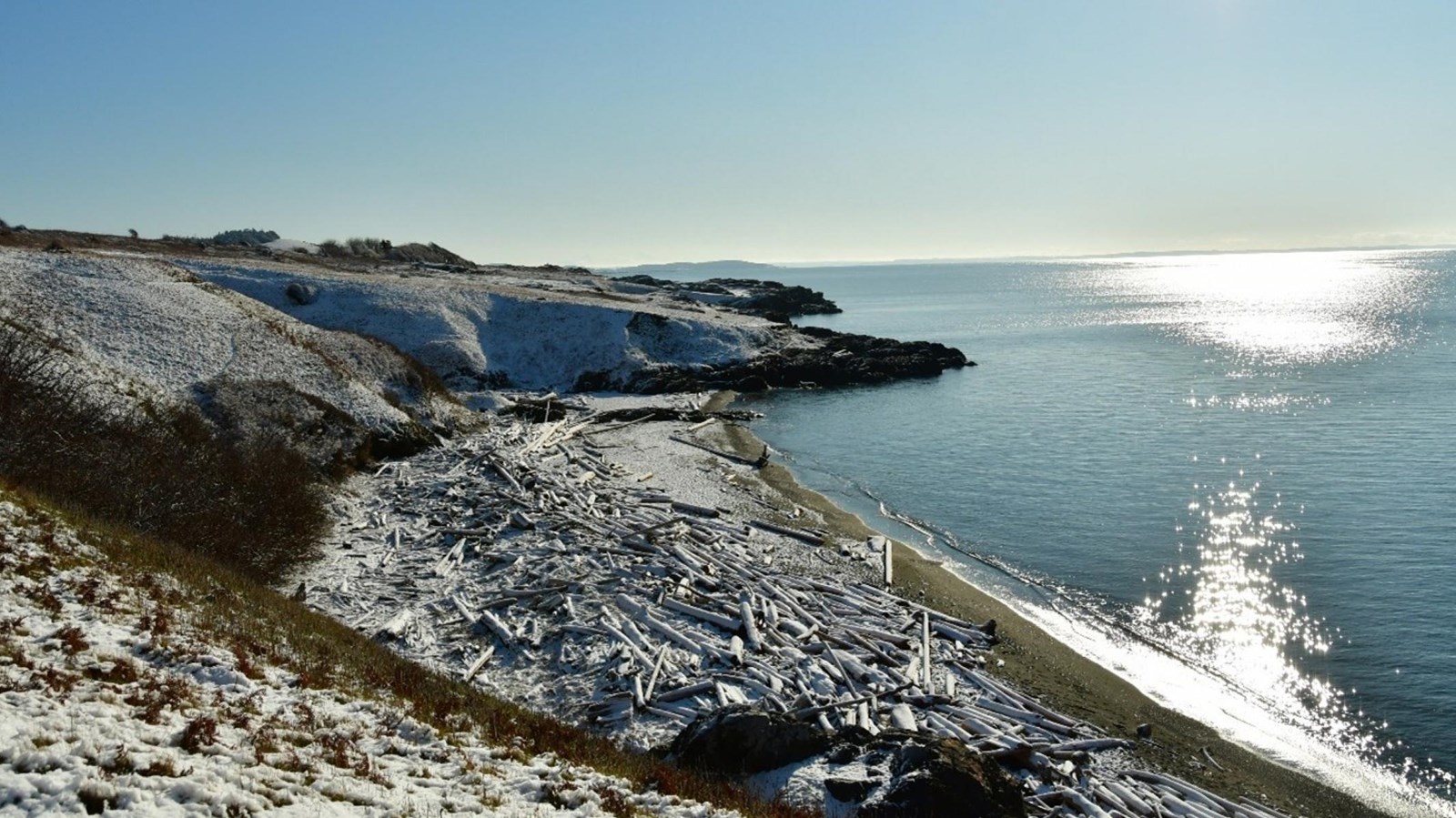 Color photograph of a sunny and snowy beach beside the ocean