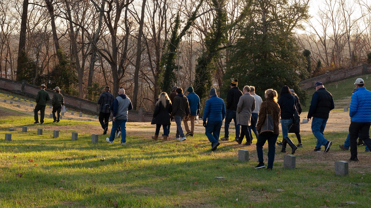 A group of visitors led by 2 park rangers in a cemetery.