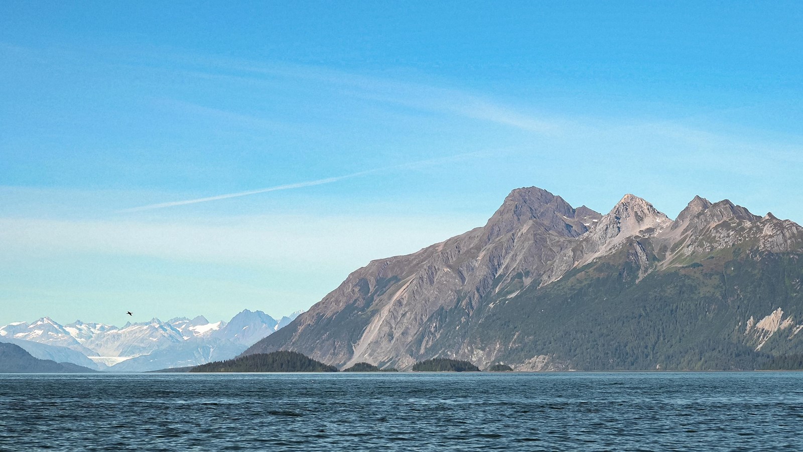 Mount Wright rises above vivid blue water on a sunny day. A glacier lies in the distance in the bay.