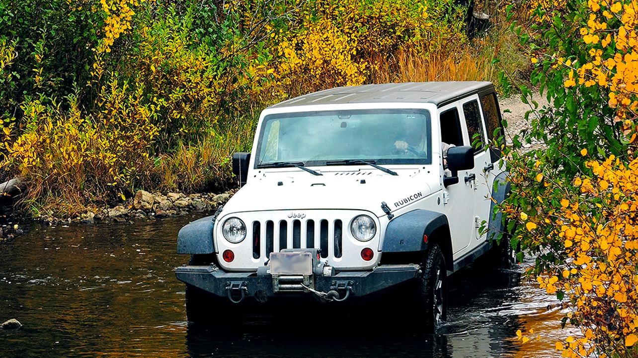 A white Jeep crosses a creek with yellow aspen trees above