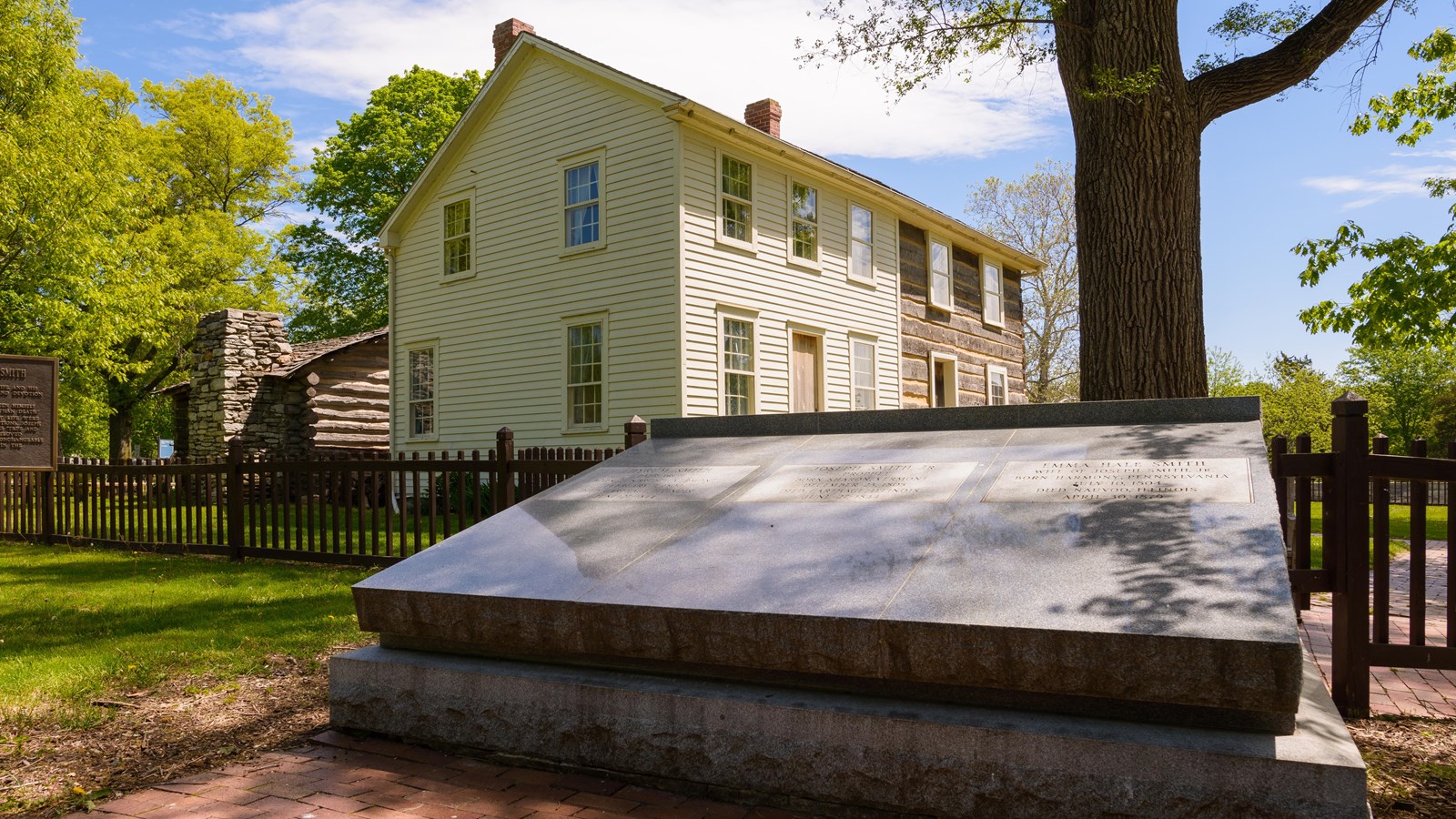 Gray granite slab in foreground. A fence surrounds a house and cabin. Trees and blue sky present.