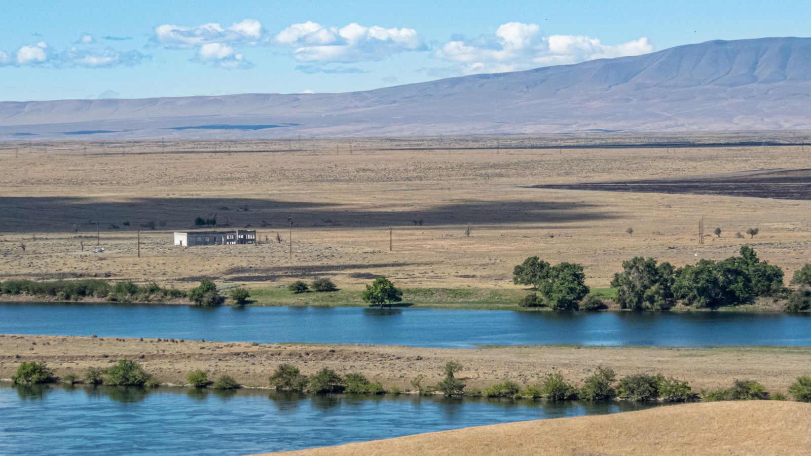 A wide panorama largely empty with low mountains in the background and brown grass in the foreground