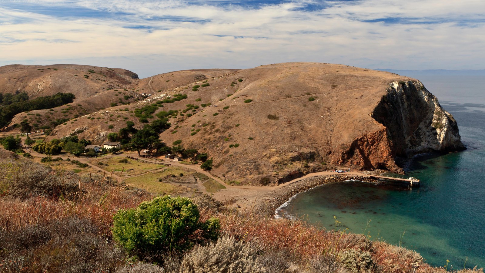 small anchorage with rocky beach, pier and ranch. 