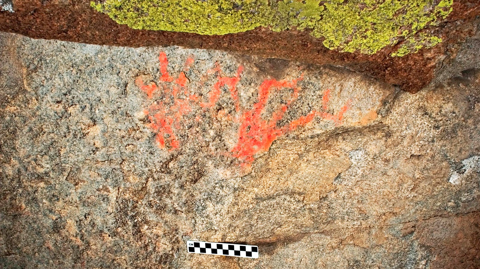 Orange colored markings on a rock that resemble hand prints.