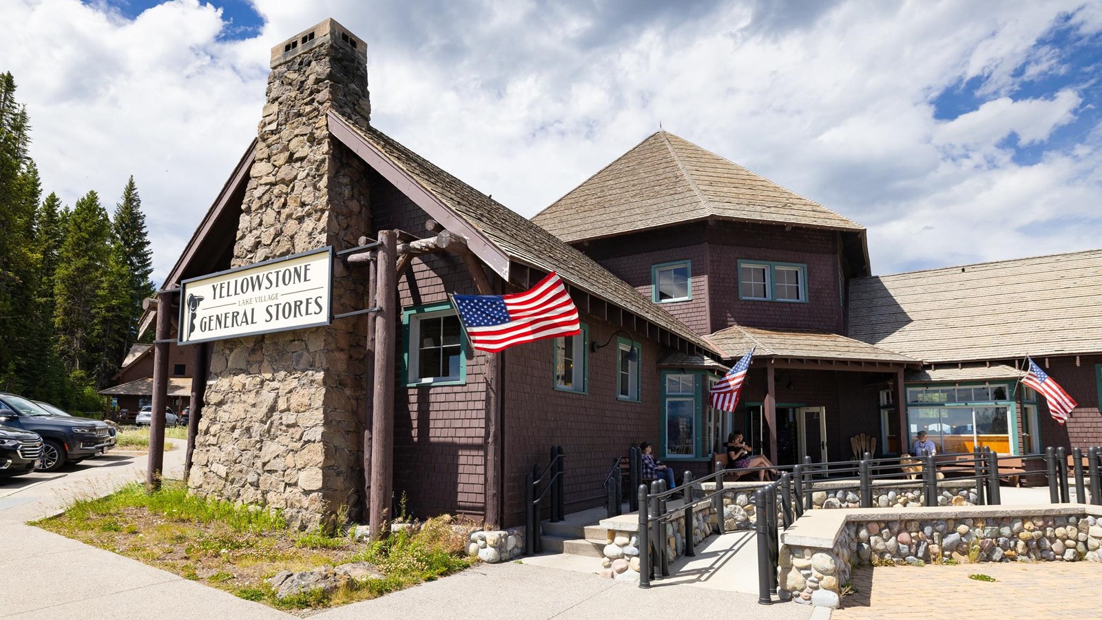 A brown, shingled building with a hexagonal roof in the center and a stone chimney.