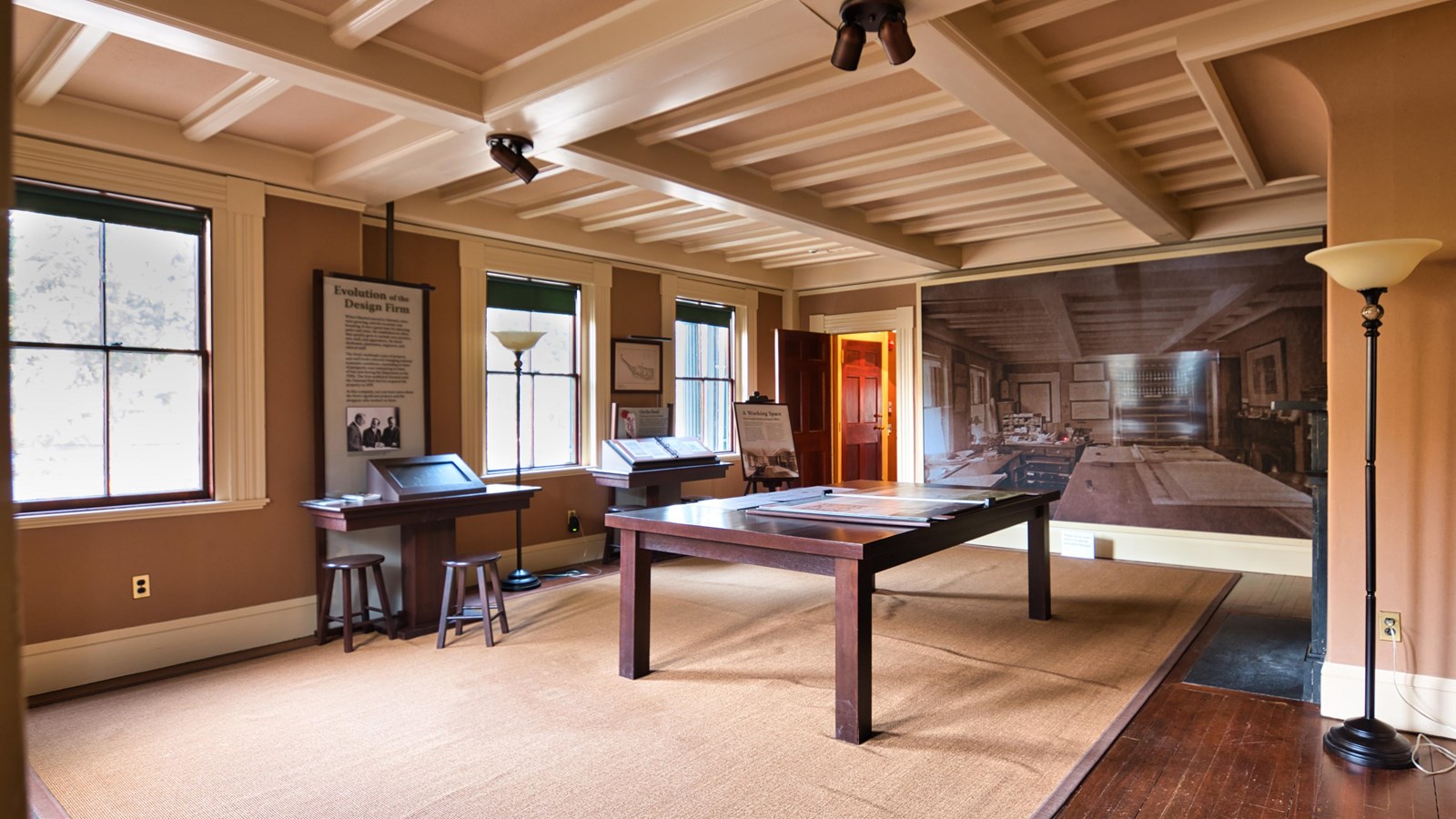 Large room with wooden desk in the middle, exhibits on one wall, and a large picture on the other