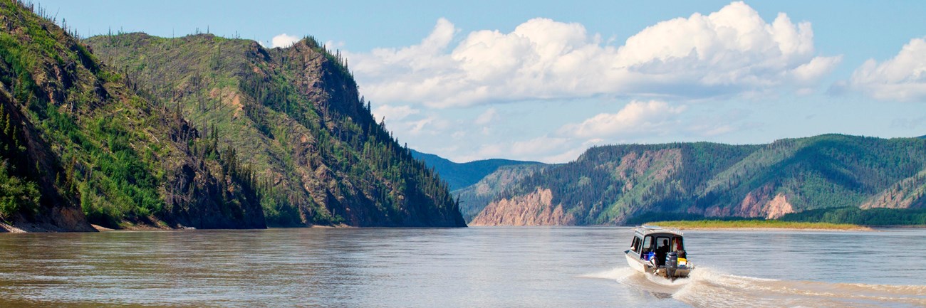 Boat traveling down the Yukon River with bluffs on each side