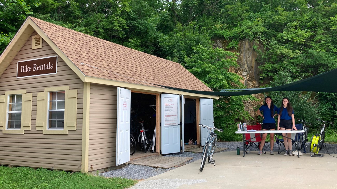 A small building containing bicycles next to an outdoor table where two people stand.