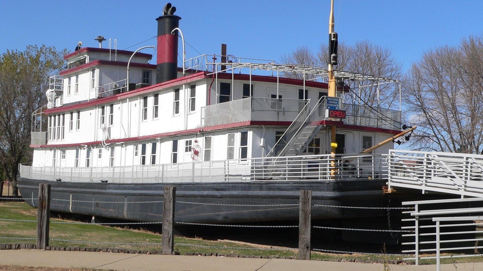 A white tow boat in front of a fence. A red and black smokestack rises from the upper deck.