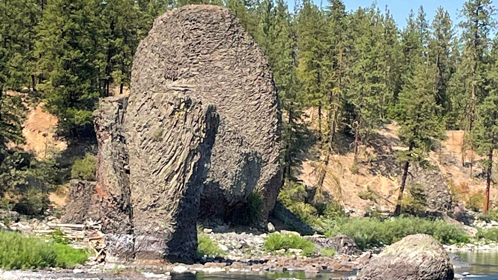Image of two large (two story tall) basalt rocks next to a stream