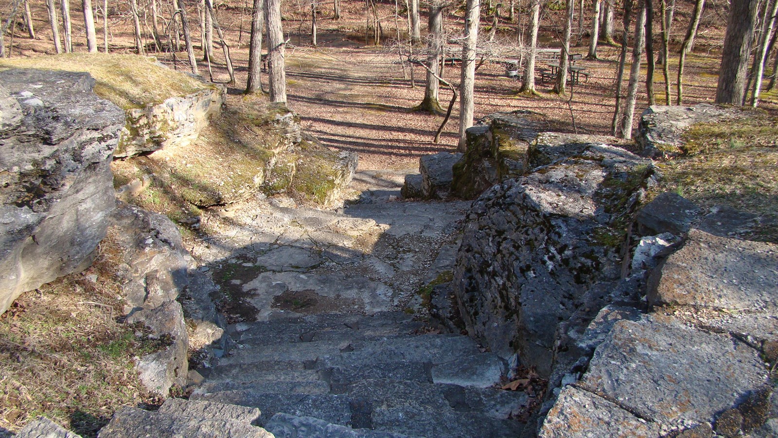 A rustic concrete stairs leading to a short trail with a stream in the distance.