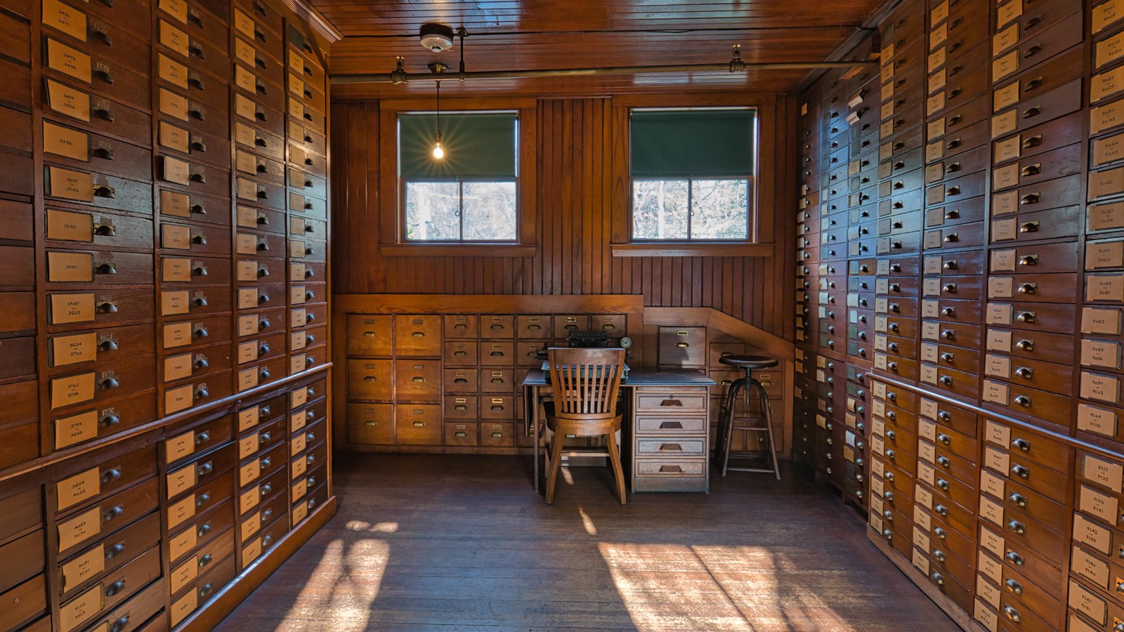 Wooden room with walls of small wooden boxes. There is a wooden desk and chair holding a typewriter.