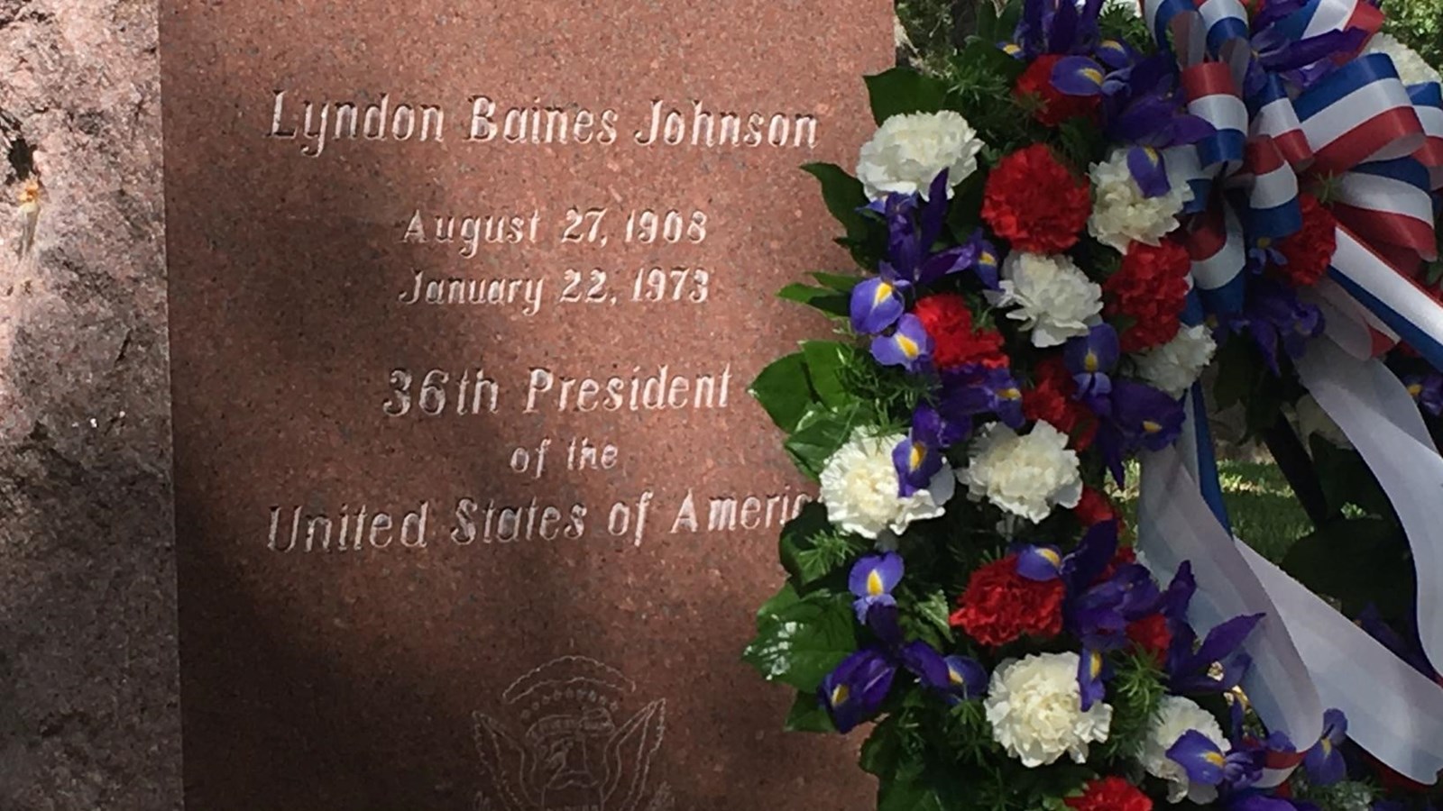 A patriotic wreath stands at the large, pink granite tombstone of President Lyndon Johnson.