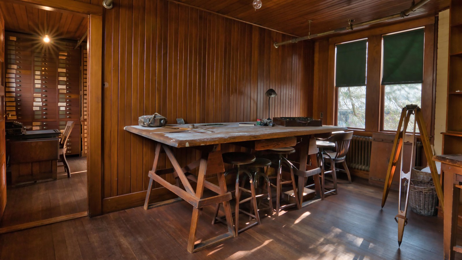 Wooden room with large wooden desk in it holding different tools. There is also a wooden tripod. 