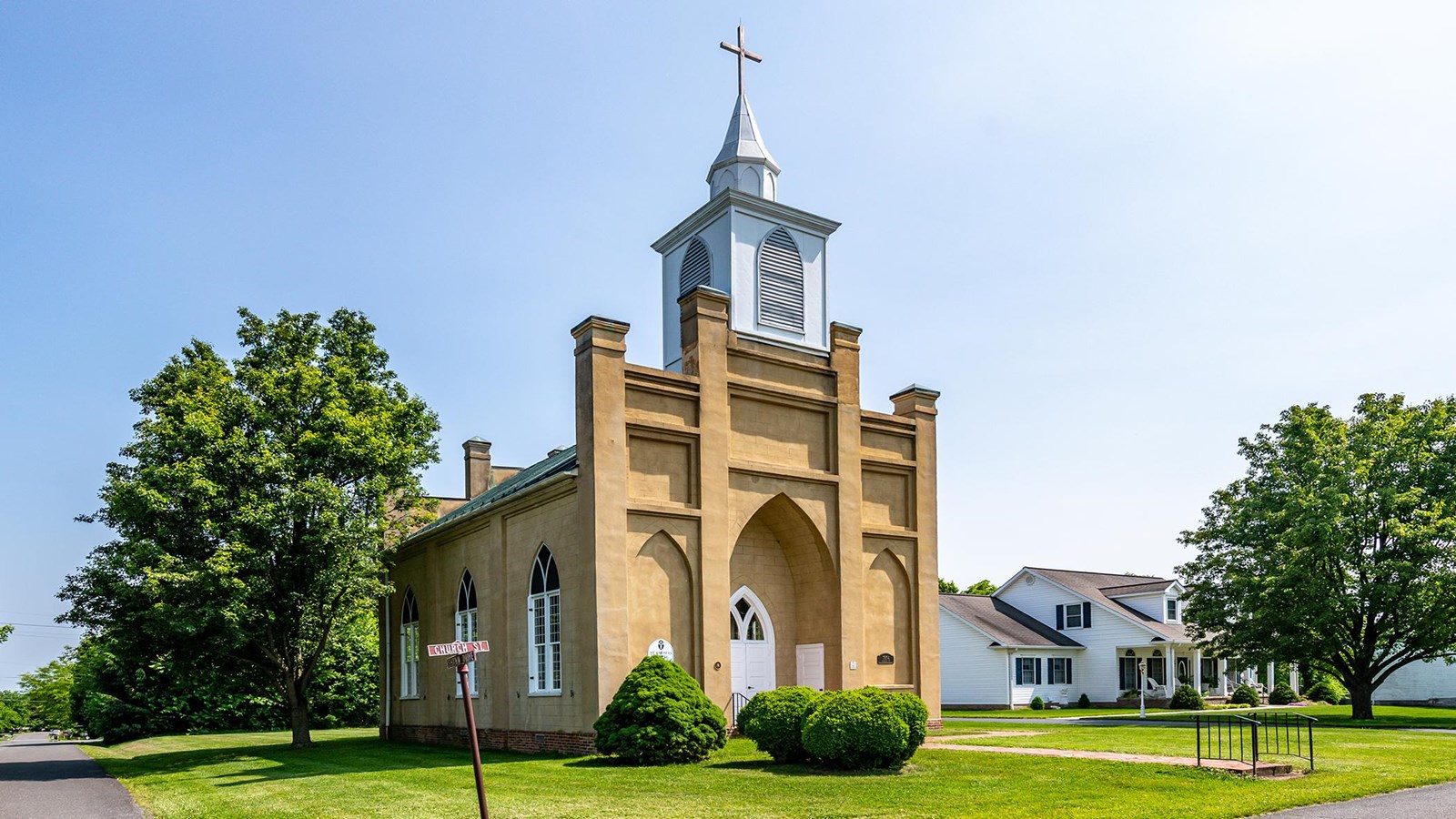A small gothic revival style church has pointed arch windows and a buff color exterior.