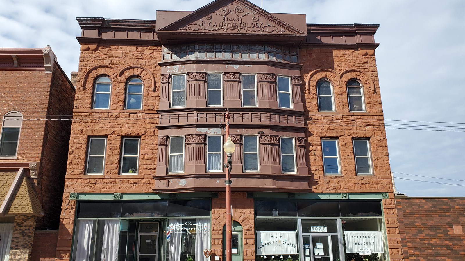 Three-story red sandstone building with metal façade and roof adornment.