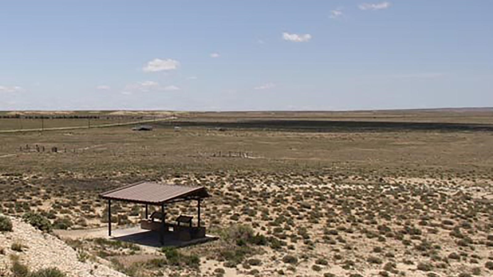 Looking out over a desert dotted with shrubs and grass, with a covered picnic area in the foreground