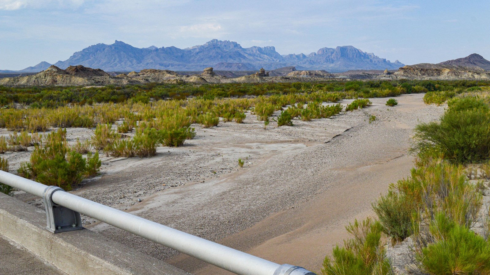 A bridge crosses a wide, dry wash with the Chisos Mountains rising in the distance.