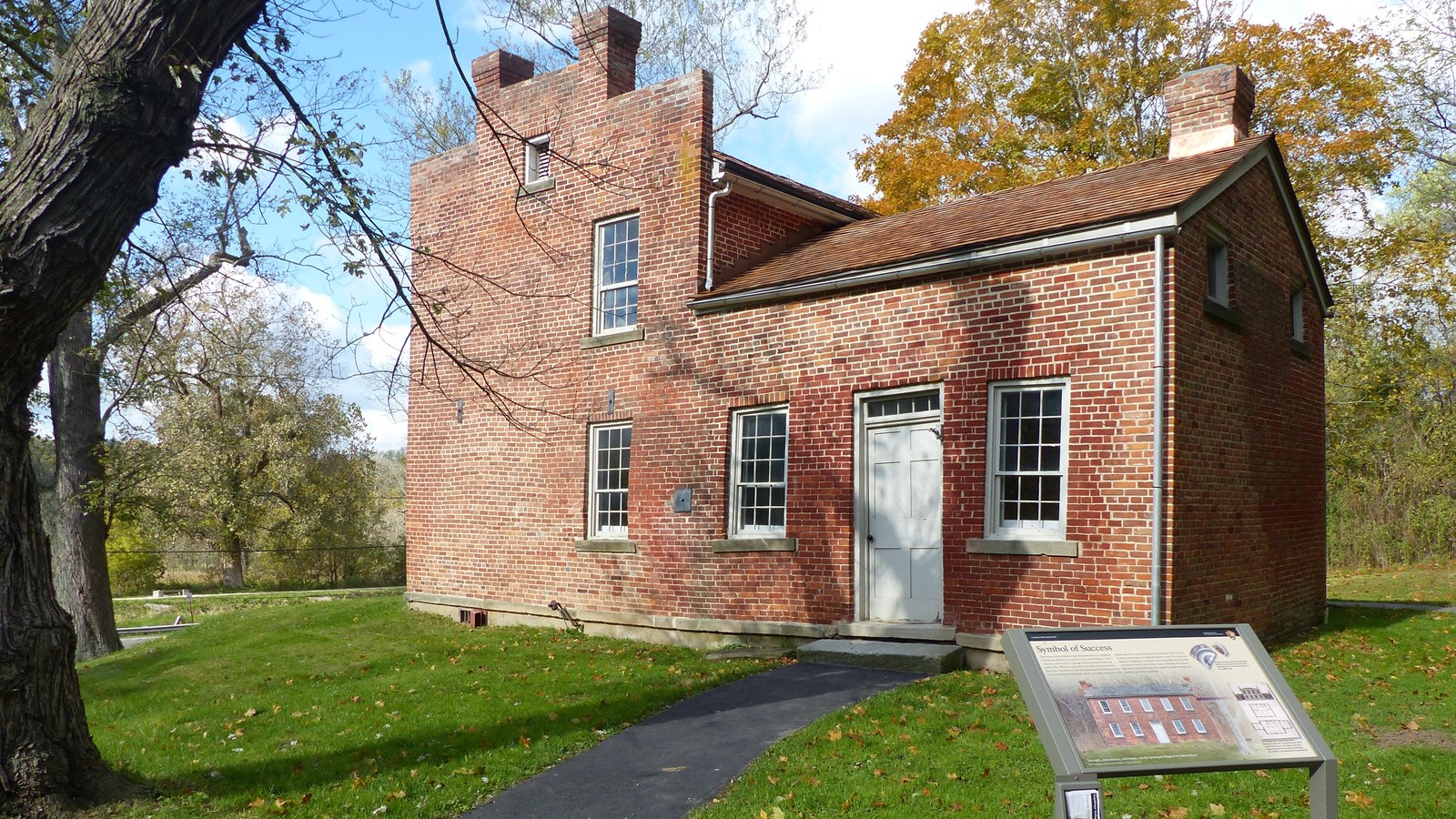 An L-shaped red brick house with four windows and white door, a graphic panel in front of it.