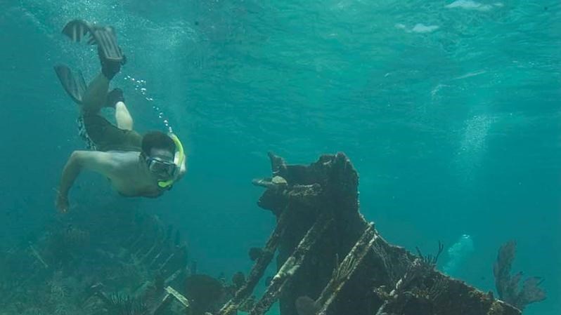 Man snorkeling a shipwreck lying on the sandy bottom of the ocean