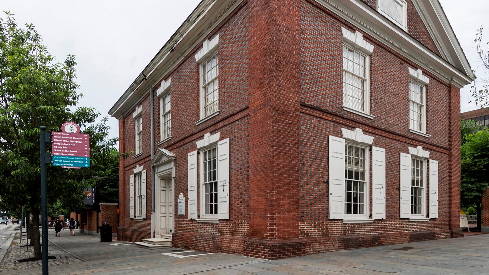 A color photo of a two story brick building on a corner property with windows and white shutters