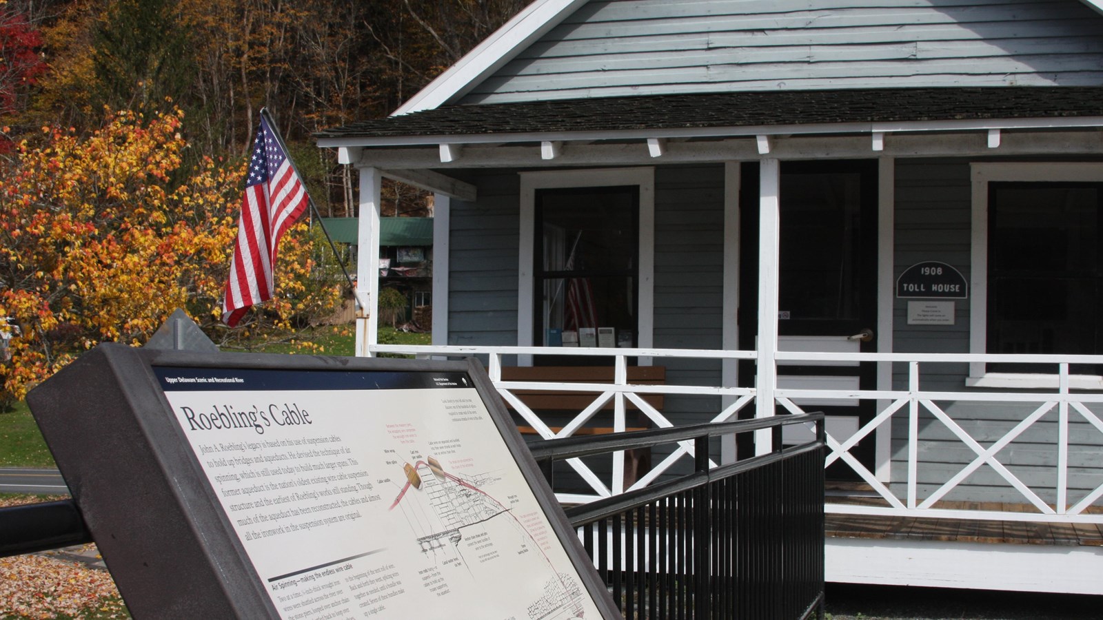 Small, light blue one-story house with white trim and white front porch with American flag.