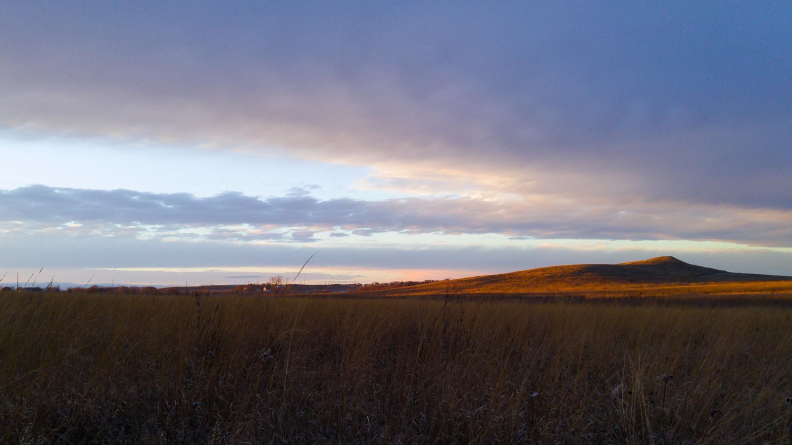 Photograph taken at dusk, with a dramatic purple sky and waves of grass. Spirit Mound is visible 